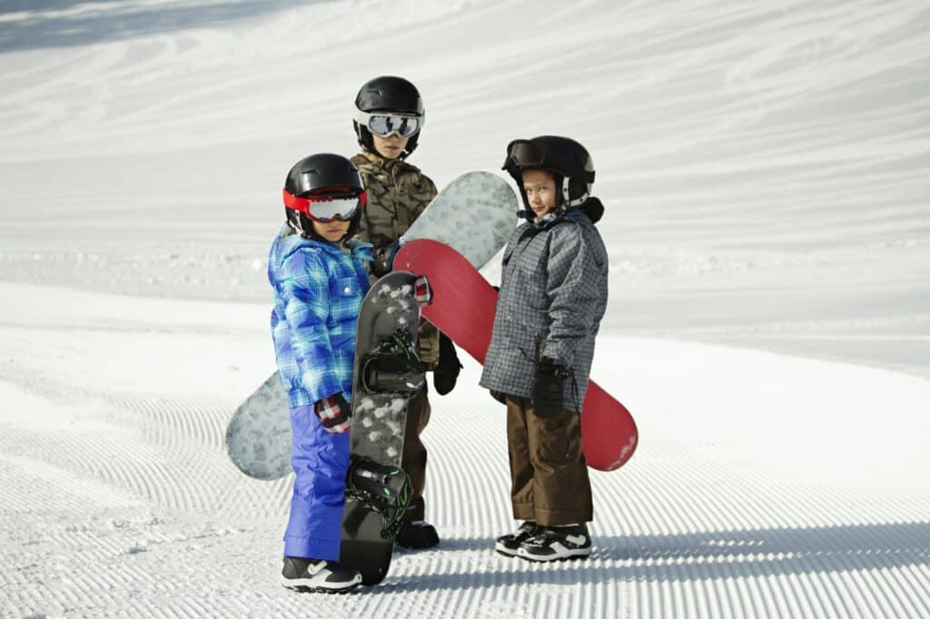 Siblings Carrying Snowboards While Standing On Snow Covered Field